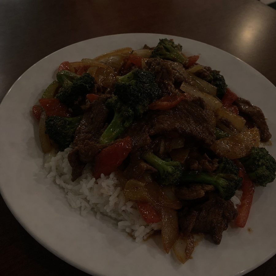 Underexposed phone photo of a beef stir fry sitting in shadow under dim restaurant lighting