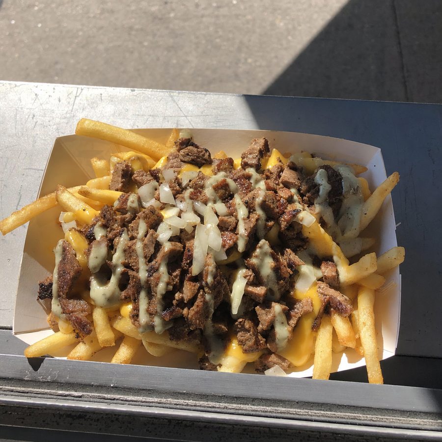 A food truck tray of loaded fries photographed in harsh sun with a hard awning shadow