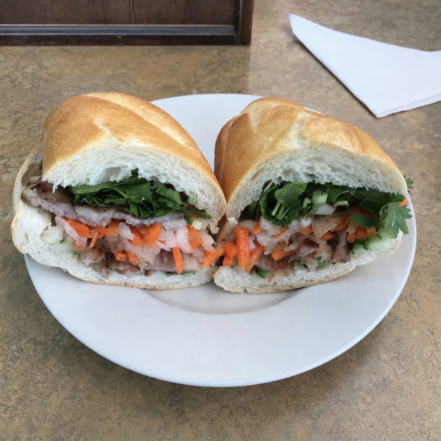 A banh mi shot in washed-out light, then balanced and evened while the pork, pickled carrot and daikon, cucumber, and cilantro in the baguette stay unchanged on the same table