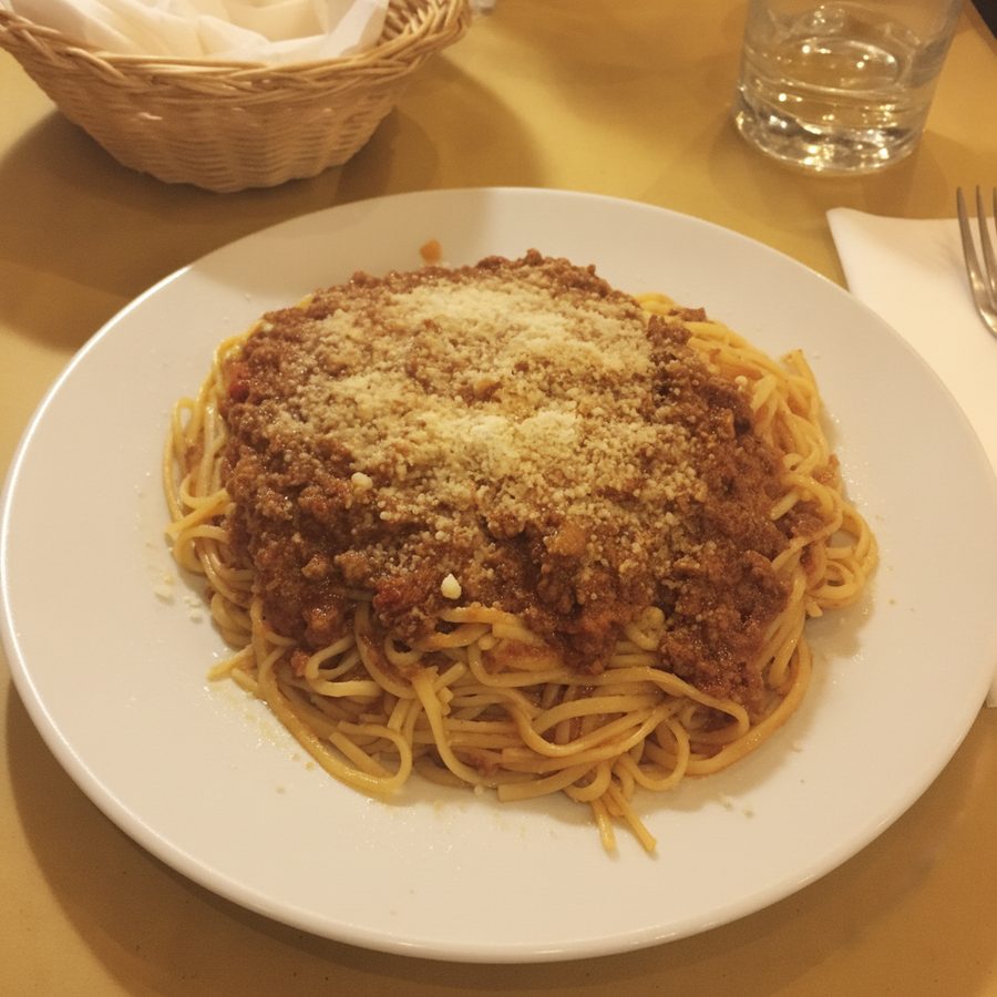 The same plate of spaghetti bolognese before and after: the warm, dim restaurant lighting corrected and brightened, with the spaghetti, meat sauce, and parmesan unchanged on the same table