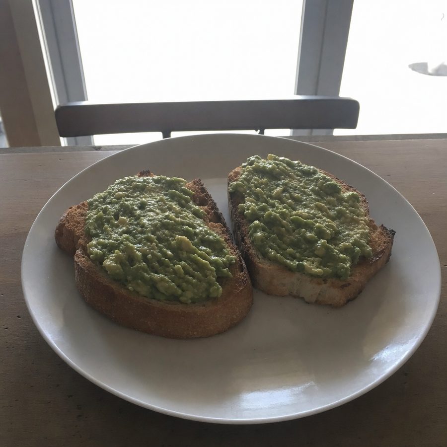 The same avocado toast before and after: harsh window backlight balanced and the plate restyled into a brighter menu photo on a warm cafe table, with the two avocado toast slices unchanged