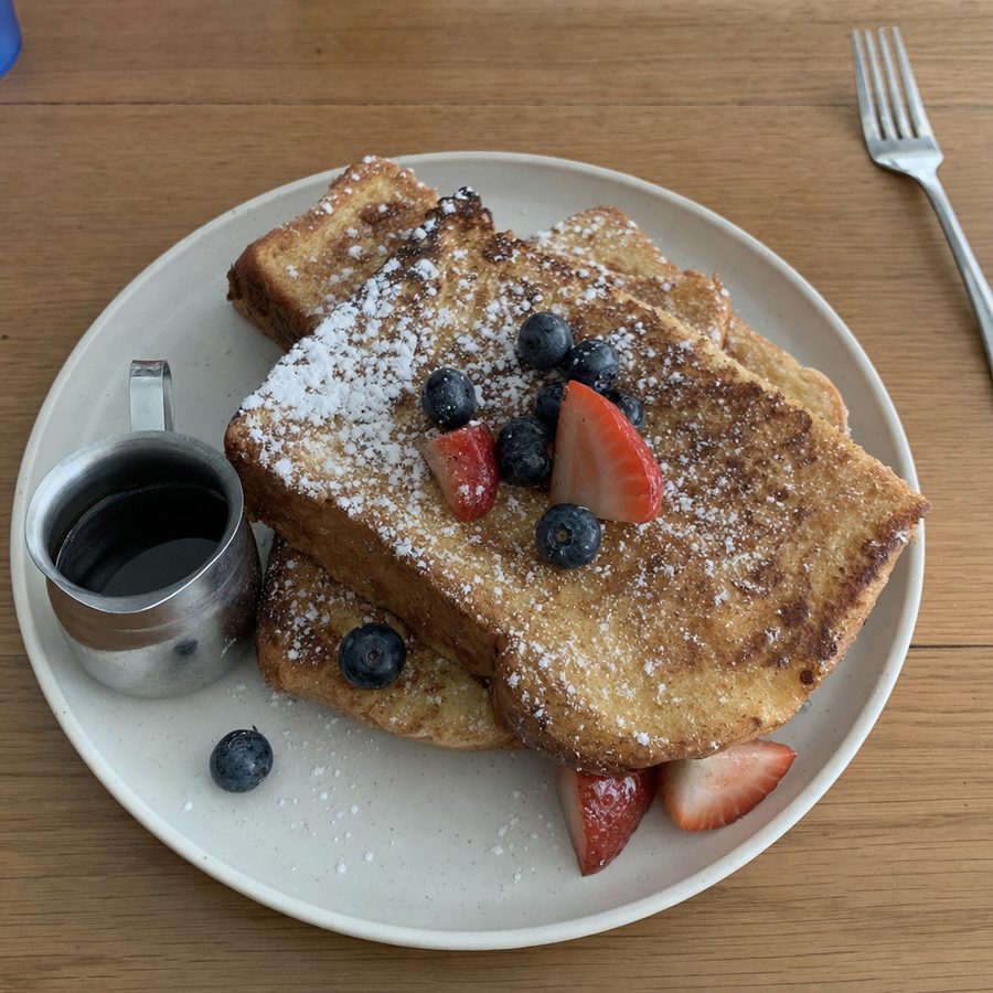 The same french toast before and after: the flat, dull lighting brightened and the color cleaned up, with the toast, powdered sugar, berries, and syrup jug unchanged on the same table