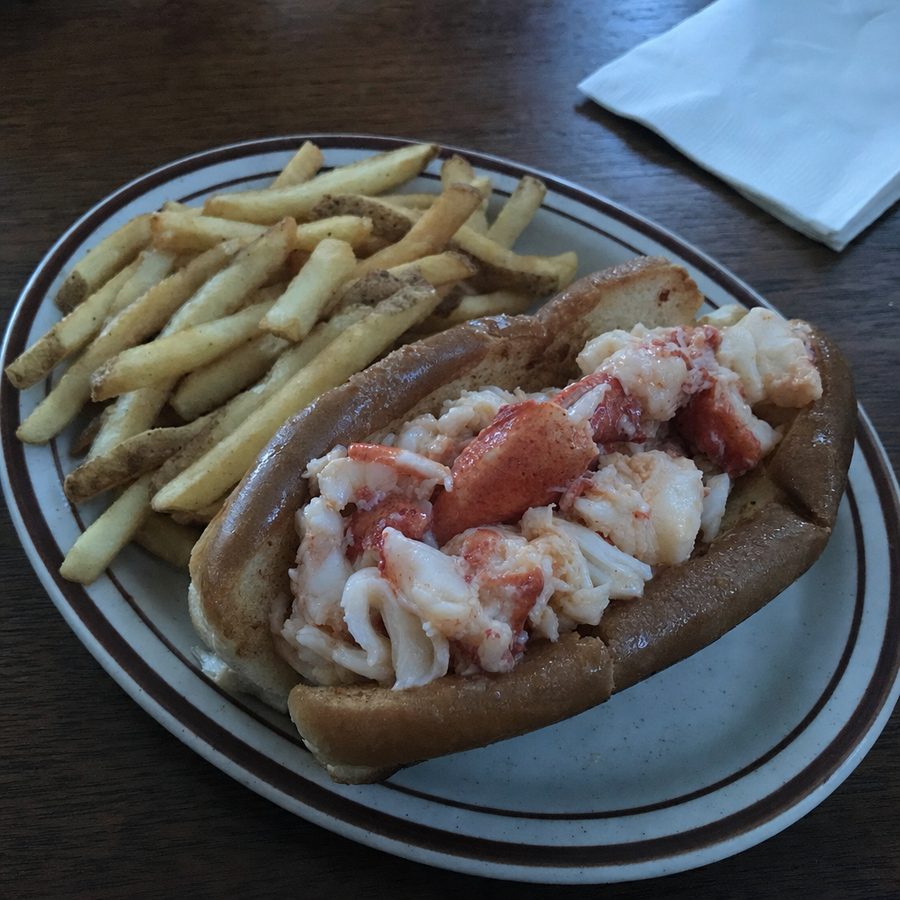 The same lobster roll before and after: the dim window light balanced and the exposure lifted, with the lobster meat, toasted bun, and fries unchanged on the same table