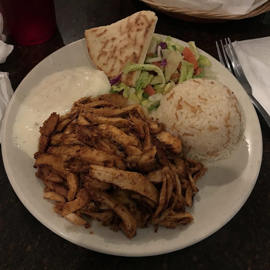 The same chicken shawarma plate before and after: the uneven, dim lighting evened out and the table tidied, with the sliced chicken, rice, salad, garlic sauce, and pita unchanged