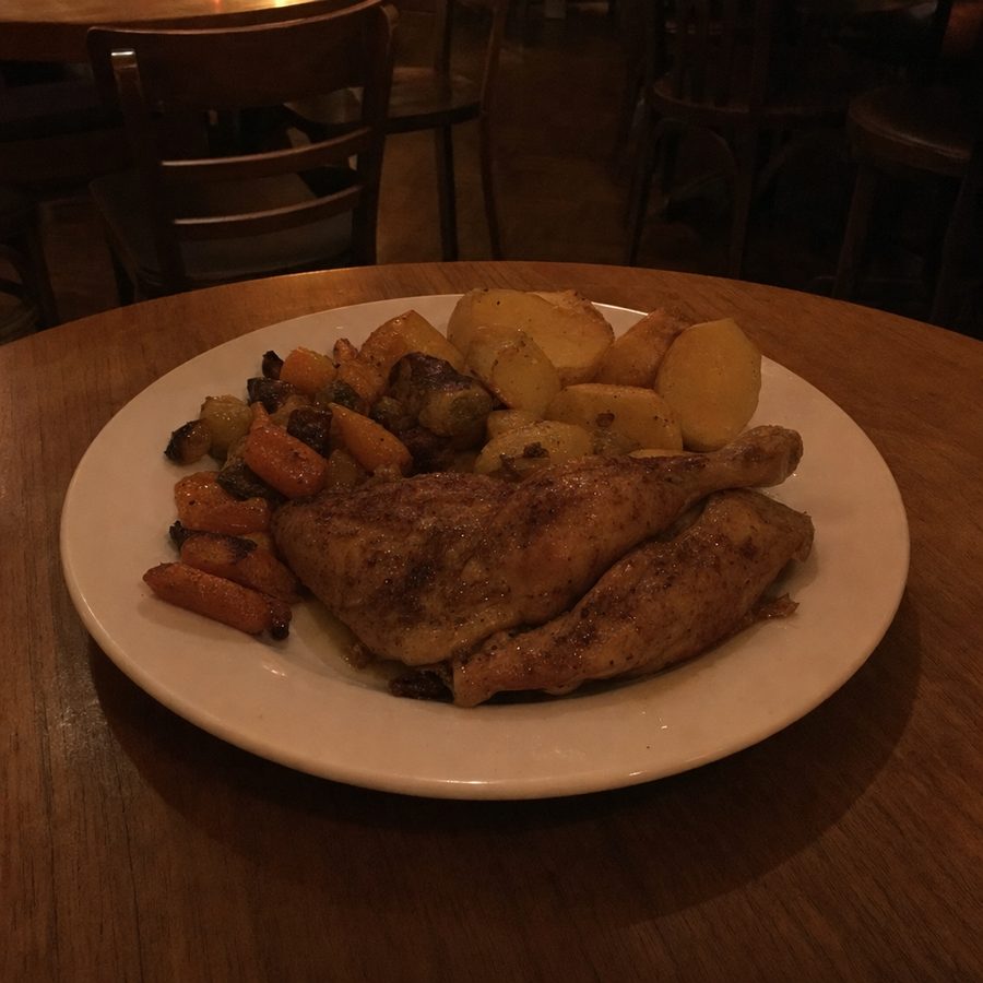 A roast chicken plate shot in a dark, warm-toned dining room before editing