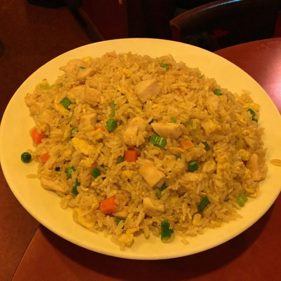 Chicken fried rice photographed under warm, murky restaurant light with a heavy orange cast