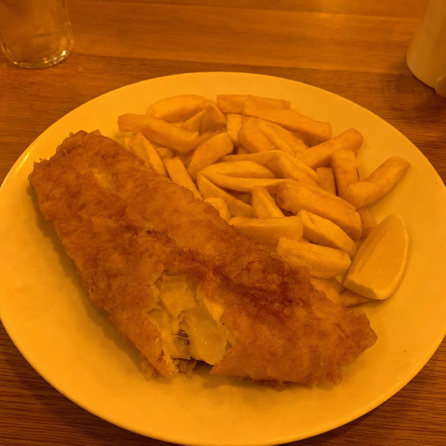 Phone photo of fish and chips with a strong yellow-orange color cast from warm restaurant lighting